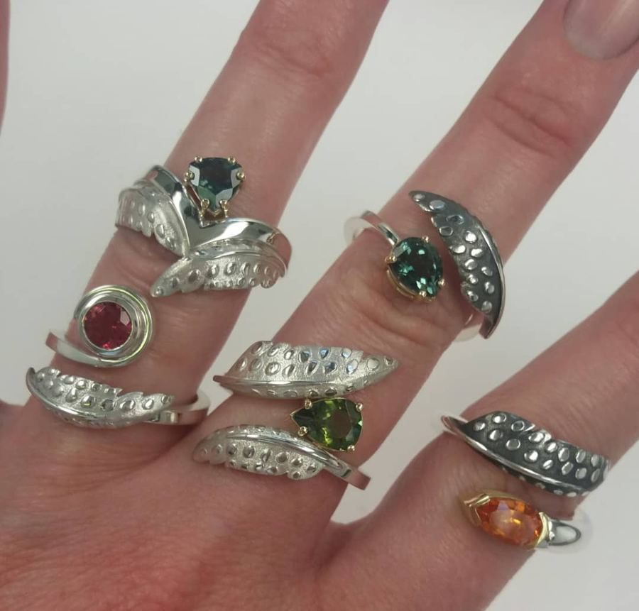 A hand wearing four of our rings with green, blue and red stones