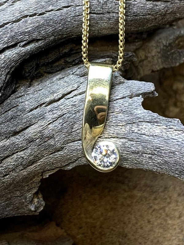 Curved gold pendant holding a round white stone, on driftwood