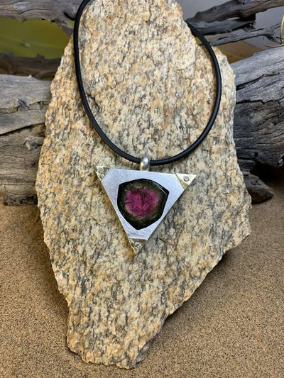 Triangular pendant with a slice of watermelon tourmaline, resting on granite