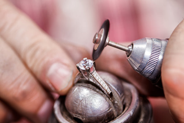 A goldsmith polishing a ring with a rotary tool at the bench