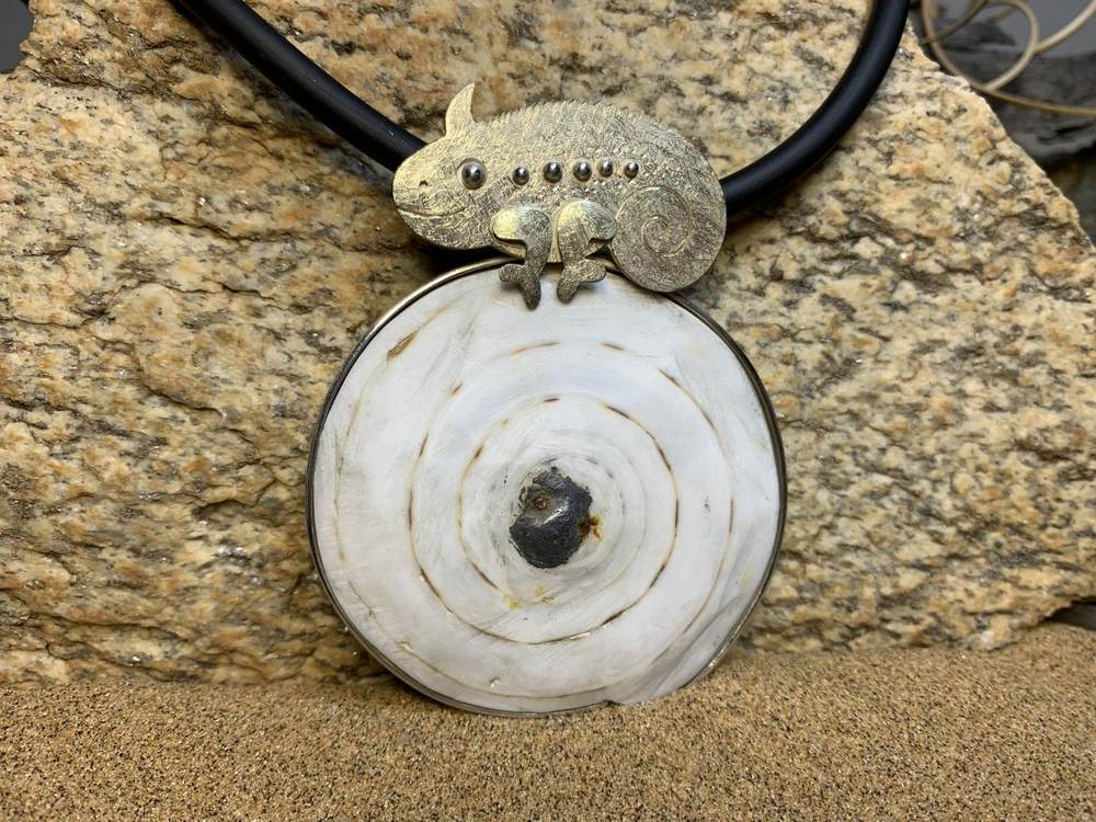 Pendant of a white Omba shell disc with a small gold chameleon, on granite