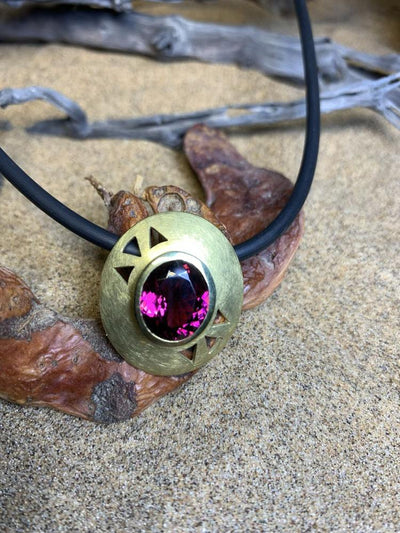 Domed gold pendant with an oval pink-purple stone, on a black cord