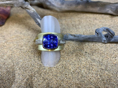 Gold ring with a cushion-cut violet-blue stone on driftwood and desert sand
